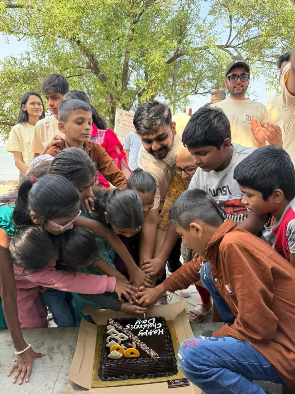Children and volunteers gathered around a Children’s Day cake, cutting it together
