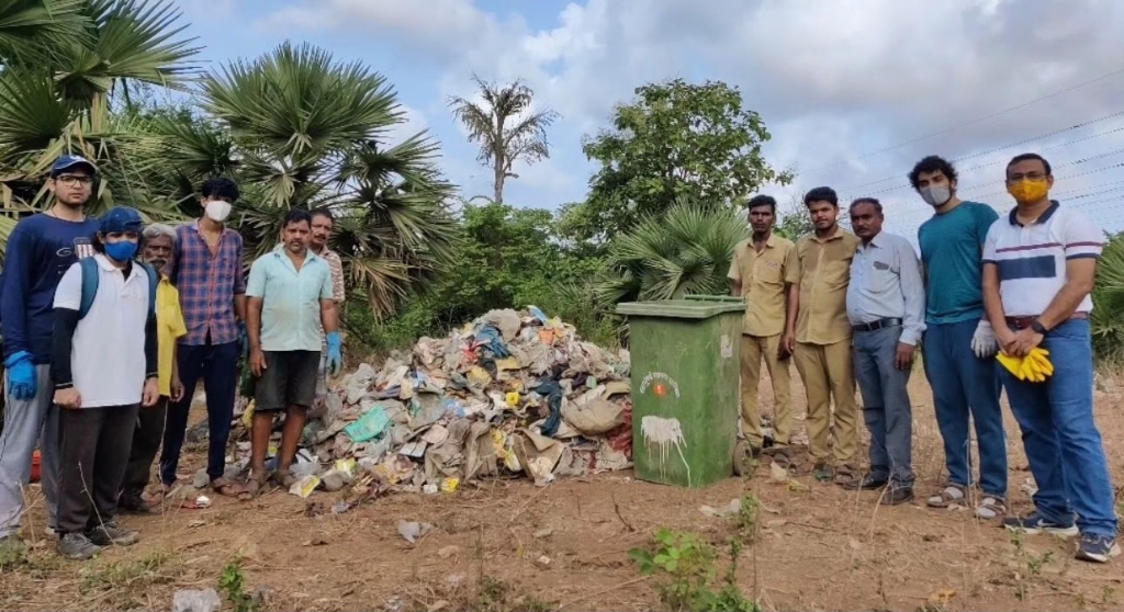 Volunteers standing beside a large pile of collected garbage and a green bin