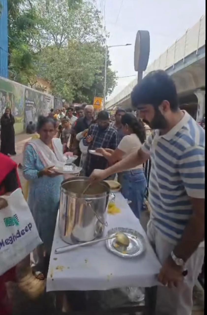 Volunteers serving hot meals from a large pot to a queue of people