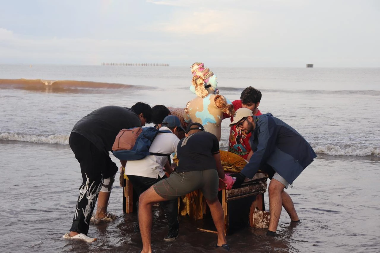 A team supporting a Ganesh idol and its base at the water’s edge